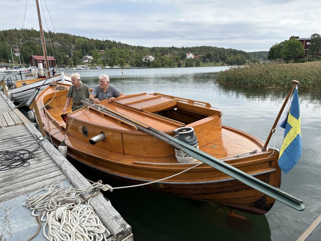 Föreningens senaste renovering, Elsie, en halvdäckad skötbåt från 1932, visas av Rolf Molin och Bengt Aronsson som senare startade Elsies maskin. Foto: Martin Prieto Beaulieu