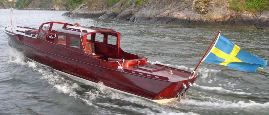 Raket i gång genom skärgårdsvatten – mahognyn glöder och den slanka Petterssonlinjen syns tydligt. När hon byggdes 1919 installerades en 30 hk Buffalo-motor; i dag, mer än hundra år senare, drivs Raket av en Mercruiser 5,7L på 300 hk. Foto: Loris Charter